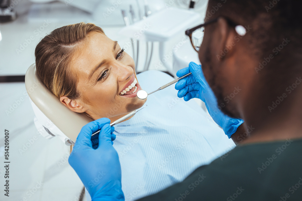 Smiling pretty woman looking with trust at dentist doctor during treatment. Beautiful young woman doing tooth examination in the dental office. Portrait of smiling girl on a dental chair in dentistry Smiling pretty woman looking with trust at dentist doctor during treatment. Beautiful young woman doing tooth examination in the dental office. Portrait of smiling girl on a dental chair in dentistry