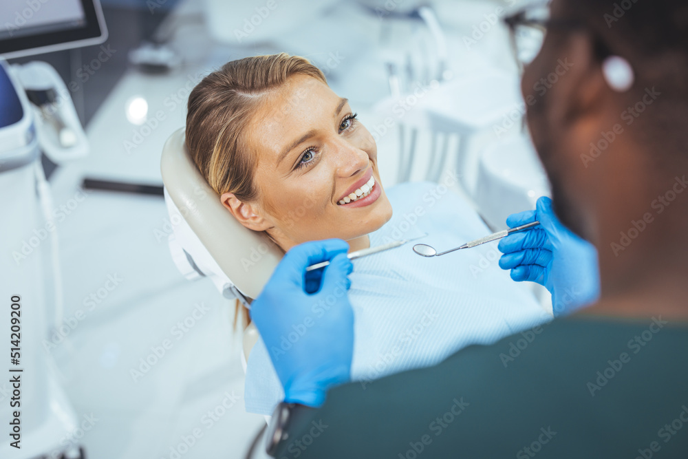 Fototapeta premium Pretty lady in dentist chair looking at her doctor with smile, close up. Image of pretty young woman sitting in dental chair at medical center while professional doctor fixing her teeth..