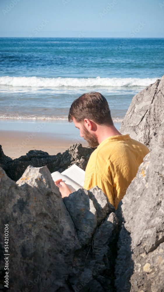 Hombre leyendo un libro en playa rocosa junto a horizonte marino