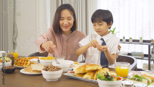 Portrait of happy smiling Asian Family eating breakfast food together before the child going to school at home. Family relationship. Love of mother  and son. People lifestyle.