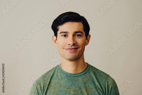 Headshot latino man black hair smiling handsome young adult green t-shirt over gray background looking at camera studio shot photo