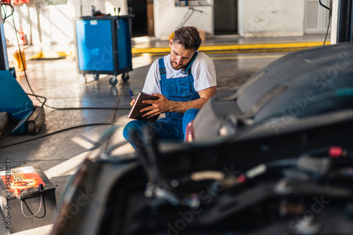 Auto mechanic communicates with client on a smart phone in a car service and writing down what he need to check.