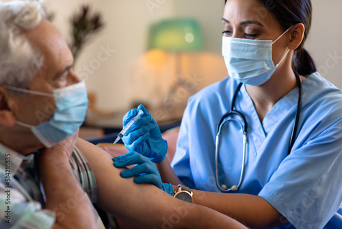 Biracial female health worker giving an injection to caucasian senior man at home