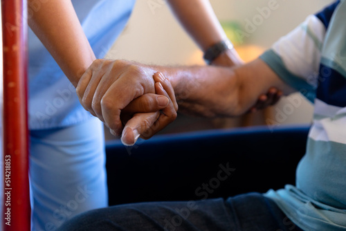 Mid section of biracial female health worker holding hand of caucasian senior man
