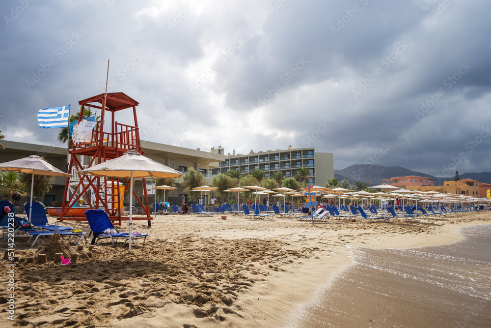 Malia, Greece - October 8, 2021: Beach chairs with umbrellas on a beautiful beach in Crete island.