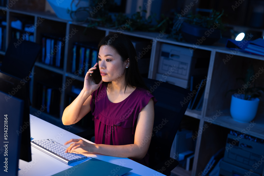 © Wavebreak Media - High angle view of asian businesswoman talking on smartphone and using computer at desk in office