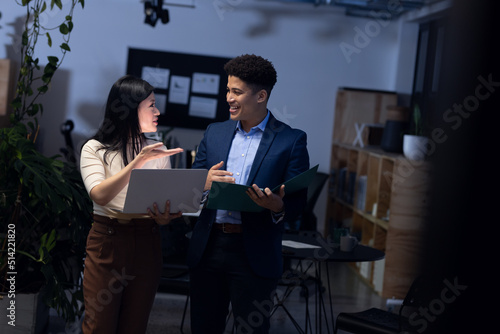 Asian male and female professionals with laptop and report discussing data in office at night photo