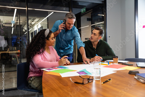 Caucasian businessman talking on smart phone while discussing with colleagues over documents