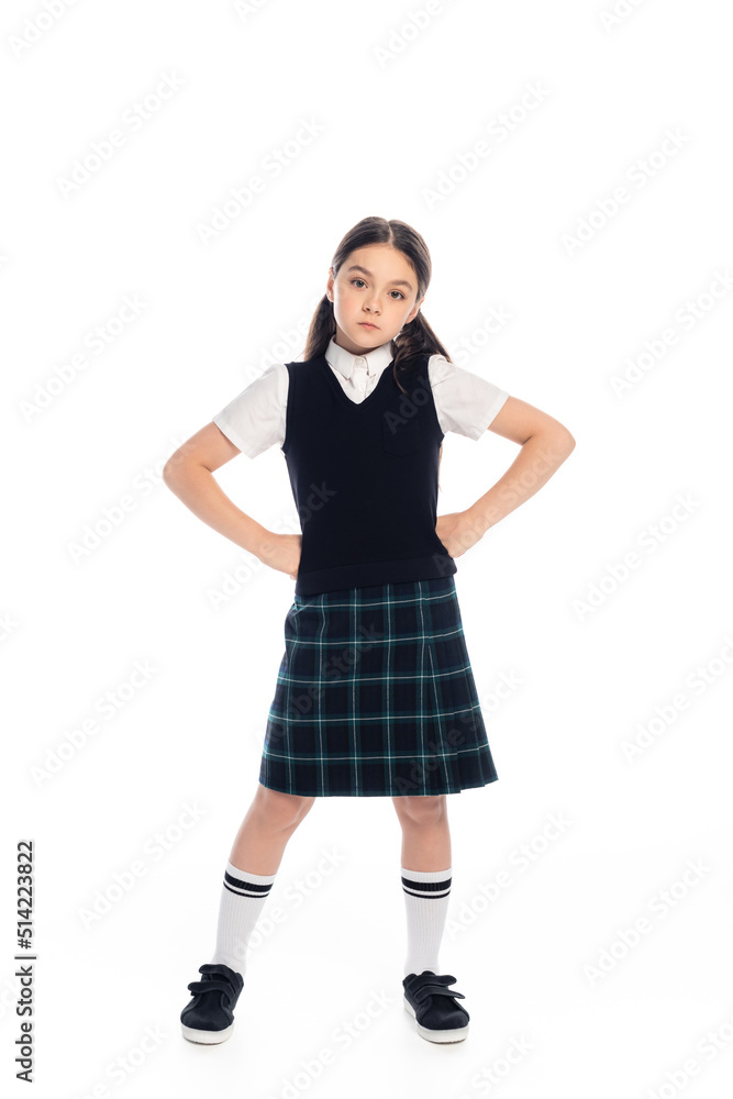 Fototapeta premium Serious schoolgirl standing in akimbo pose on white background.