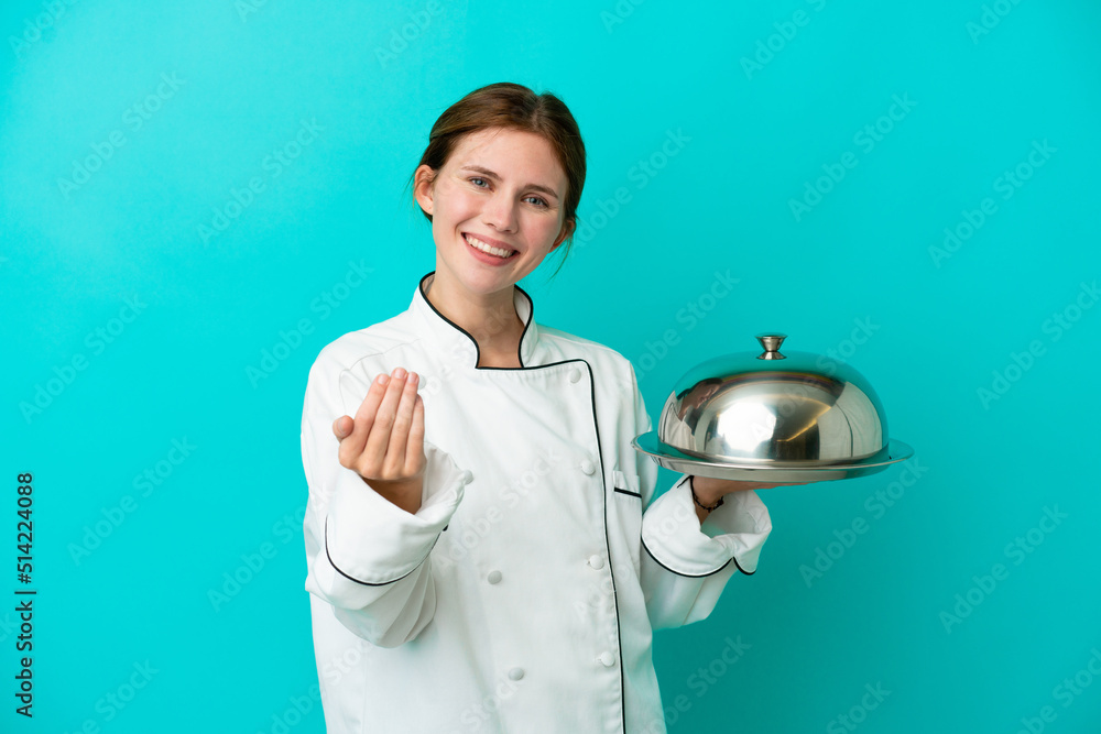 Young chef woman with tray isolated on blue background inviting to come with hand. Happy that you came Young chef woman with tray isolated on blue background inviting to come with hand. Happy that you came