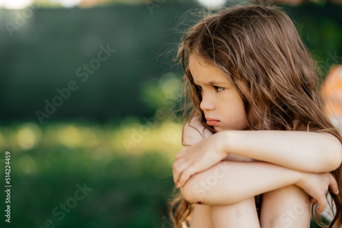 little offended girl sits with a sad expression hugging her knees photo