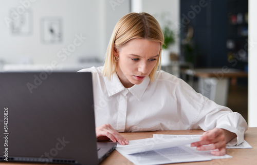 Young woman working with laptop and documents.