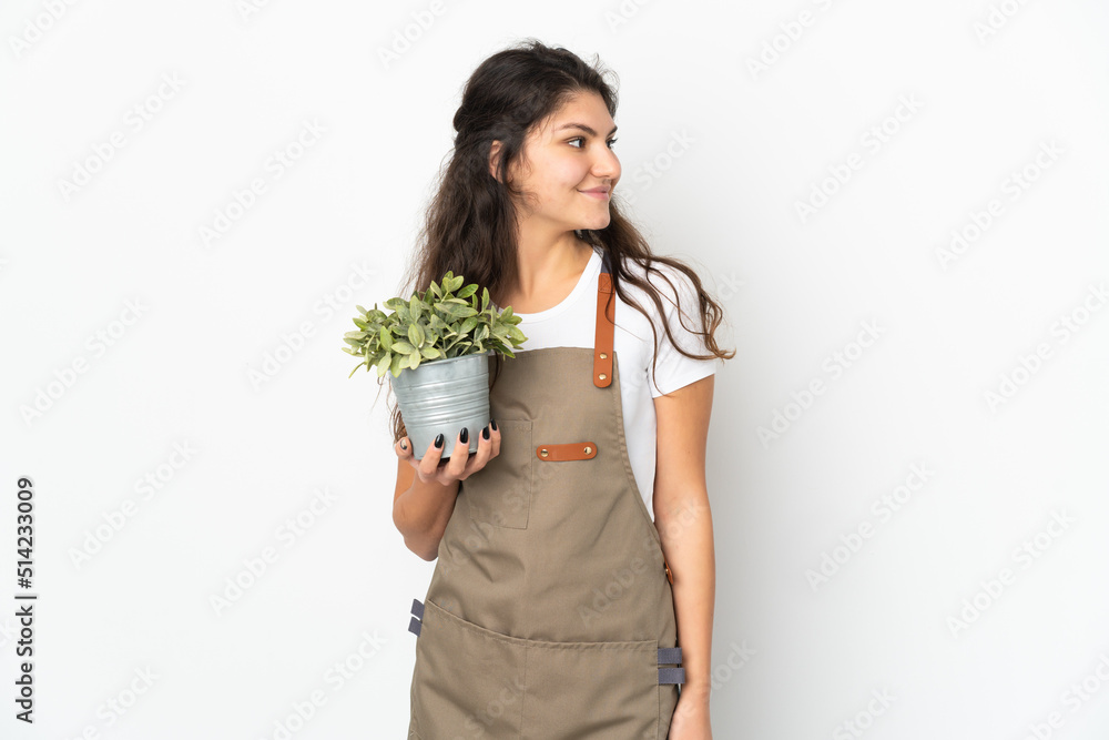 Young Russian gardener girl holding a plant isolated looking side Young Russian gardener girl holding a plant isolated looking side