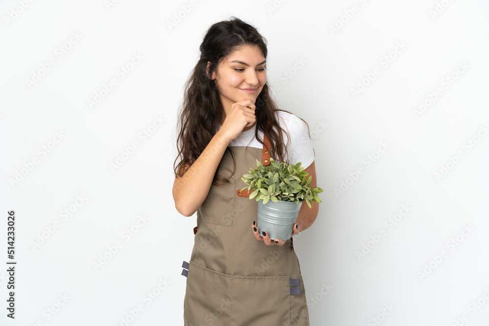 Young Russian gardener girl holding a plant isolated looking to the side and smiling Young Russian gardener girl holding a plant isolated looking to the side and smiling