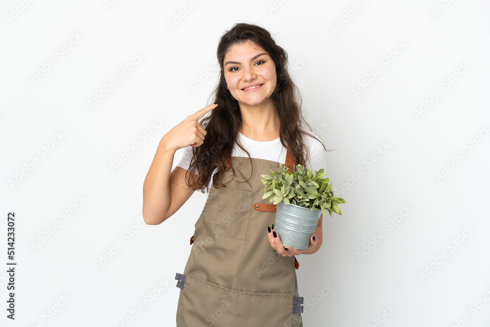 Young Russian gardener girl holding a plant isolated giving a thumbs up gesture Young Russian gardener girl holding a plant isolated giving a thumbs up gesture