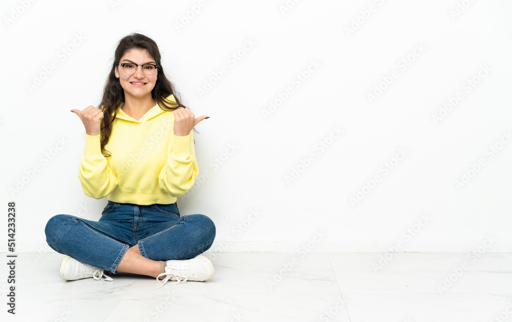 Teenager Russian girl sitting on the floor with thumbs up gesture and smiling Teenager Russian girl sitting on the floor with thumbs up gesture and smiling