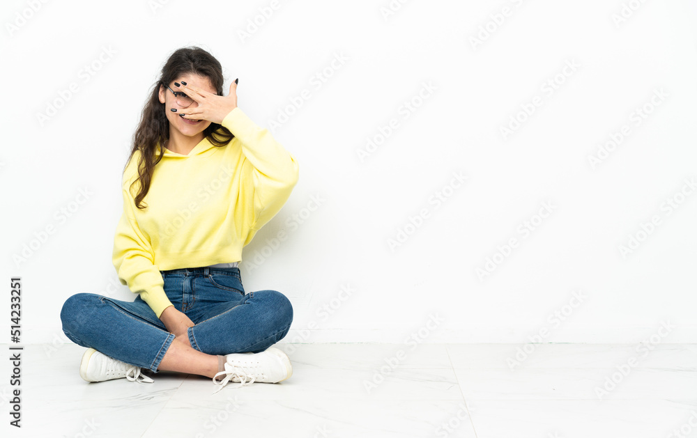 Teenager Russian girl sitting on the floor covering eyes by hands and smiling Teenager Russian girl sitting on the floor covering eyes by hands and smiling