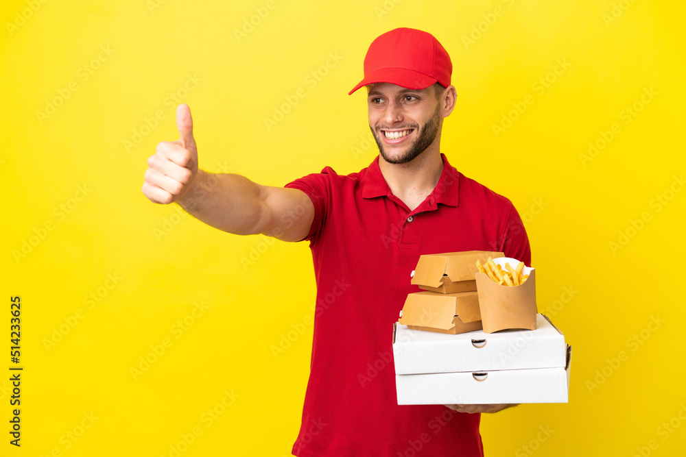 pizza delivery man picking up pizza boxes and burgers over isolated background giving a thumbs up gesture pizza delivery man picking up pizza boxes and burgers over isolated background giving a thumbs up gesture