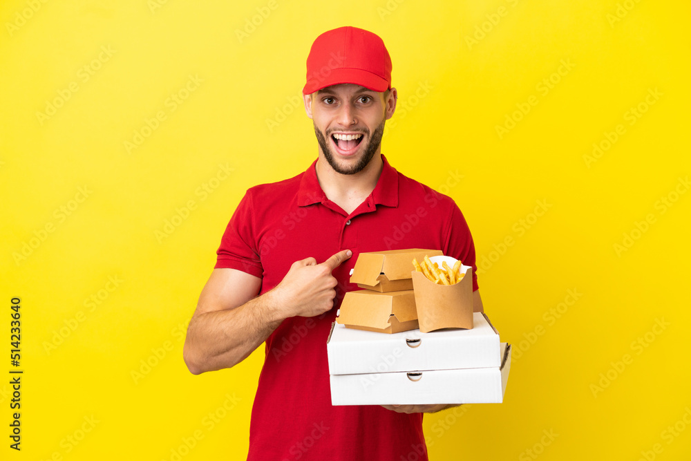 pizza delivery man picking up pizza boxes and burgers over isolated background with surprise facial expression pizza delivery man picking up pizza boxes and burgers over isolated background with surprise facial expression