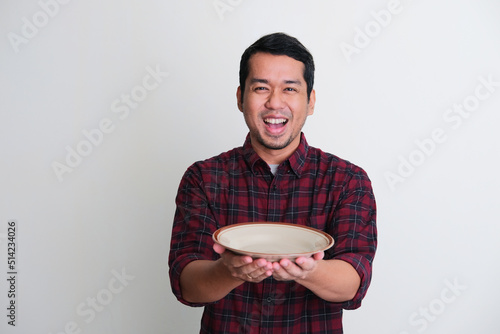 Adult Asian man showing enthusiastic expression while holding empty dinner plate