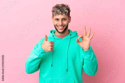 Young handsome caucasian man isolated on pink background showing ok sign and thumb up gesture