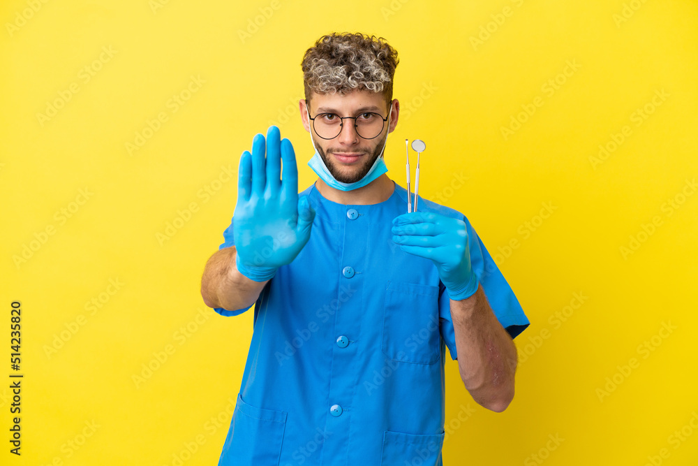 Dentist caucasian man holding tools isolated on yellow background making stop gesture Dentist caucasian man holding tools isolated on yellow background making stop gesture