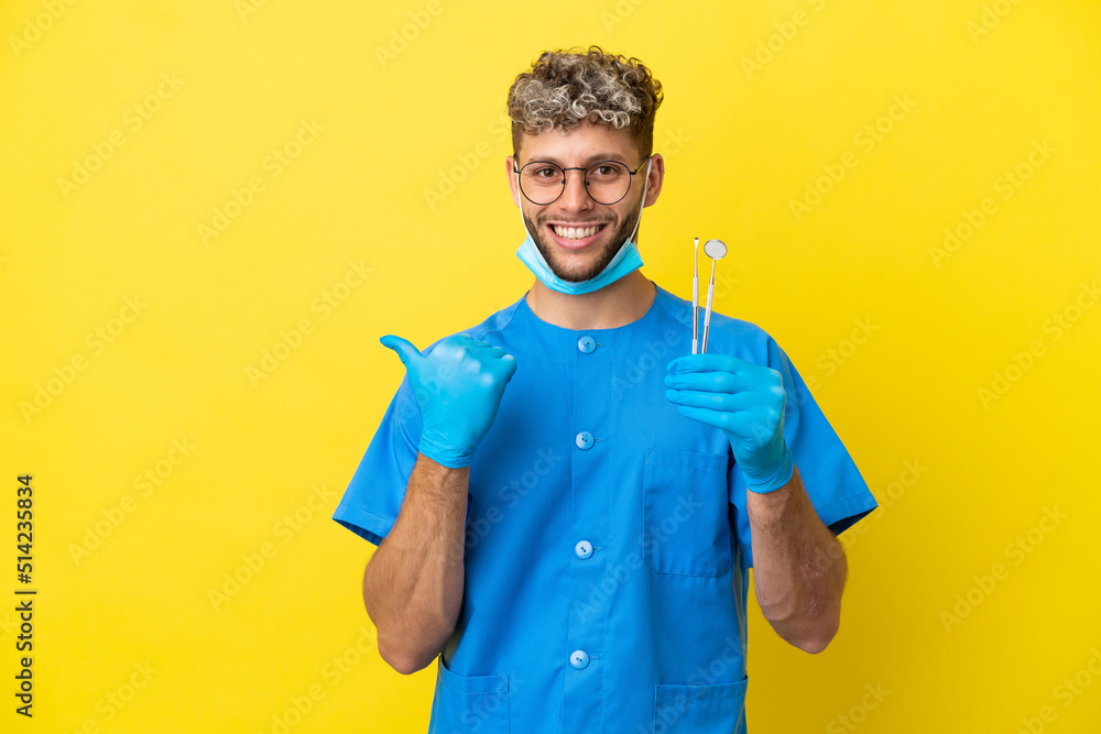 Dentist caucasian man holding tools isolated on yellow background pointing to the side to present a product Dentist caucasian man holding tools isolated on yellow background pointing to the side to present a product
