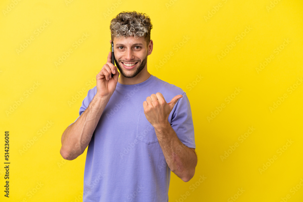 Young caucasian man using mobile phone isolated on yellow background pointing to the side to present a product Young caucasian man using mobile phone isolated on yellow background pointing to the side to present a product