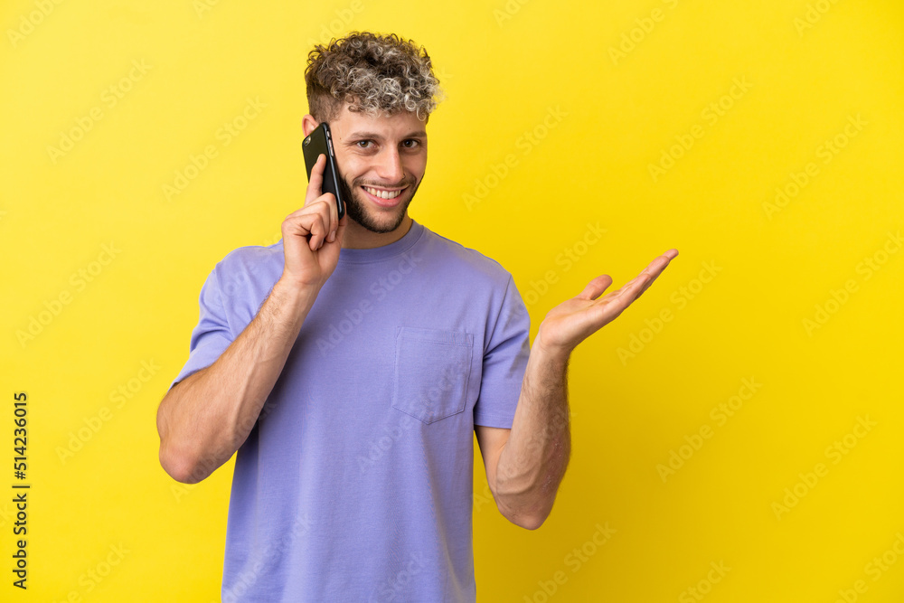 Young caucasian man using mobile phone isolated on yellow background extending hands to the side for inviting to come Young caucasian man using mobile phone isolated on yellow background extending hands to the side for inviting to come