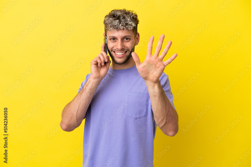 Young caucasian man using mobile phone isolated on yellow background counting five with fingers Young caucasian man using mobile phone isolated on yellow background counting five with fingers