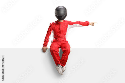 Full length portrait of a racer with a helmet sitting on a blank panel and pointing