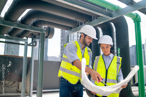 Couple professional engineer discuss with blue print of construction site and stay under the floating pipe or pipe hanging on deck of building.
