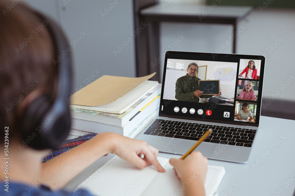 Caucasian boy wearing headphones writing in book while studying online over video call on laptop Caucasian boy wearing headphones writing in book while studying online over video call on laptop