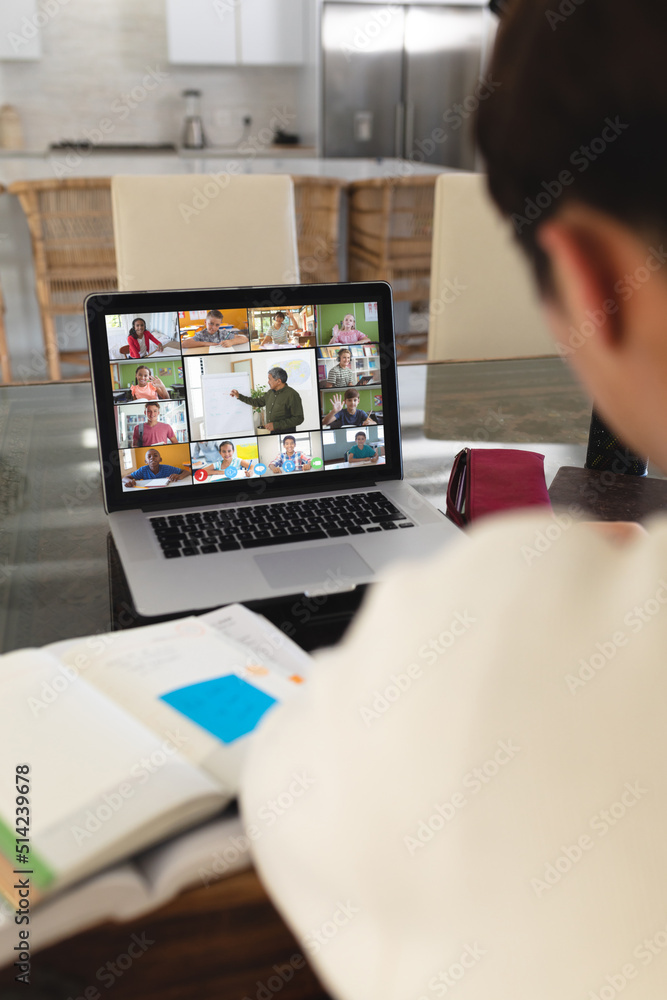 © vectorfusionart - Asian teenage boy with books on table studying online through video call on laptop at home
