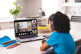 Biracial boy with curly hair looking at teacher teaching online over video call on laptop at home