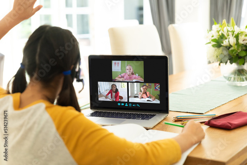 Rear view of caucasian girl raising hand during online class over video call on laptop at home