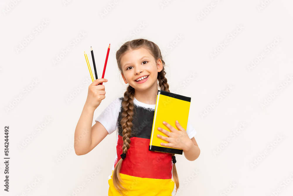 A little girl with a German flag on her T-shirt holds a book and pencils on a white isolated background. German language courses for schoolchildren. A little girl with a German flag on her T-shirt holds a book and pencils on a white isolated background. German language courses for schoolchildren.