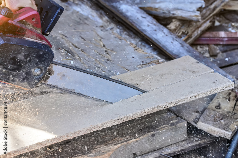 Cutting old wooden chipboards with electric chainsaw, splinters flying in air, closeup detail Cutting old wooden chipboards with electric chainsaw, splinters flying in air, closeup detail