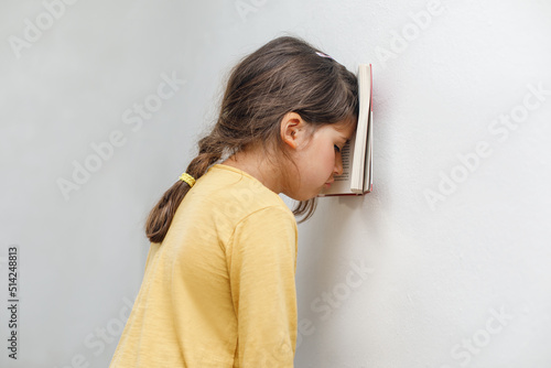 Sad and tired caucasian girl with dyslexia holds a wall. The child learns to speak and read correctly photo