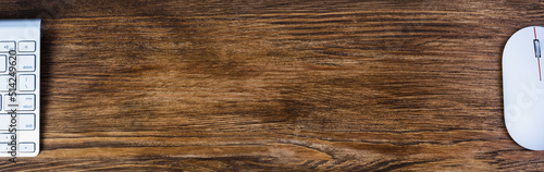 Wide banner with space for text. Top view of a mouse and keyboard on a wooden brown table.