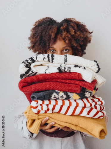 A woman peeks out from behind a pile of warm clothes.