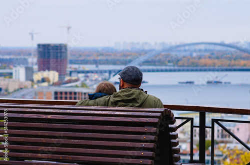 Romantic couple on bench.Couple in love sitting on the wooden bench and looks to the cityscape of autumn Kyiv. Romantic scene. Dating concept. Back view