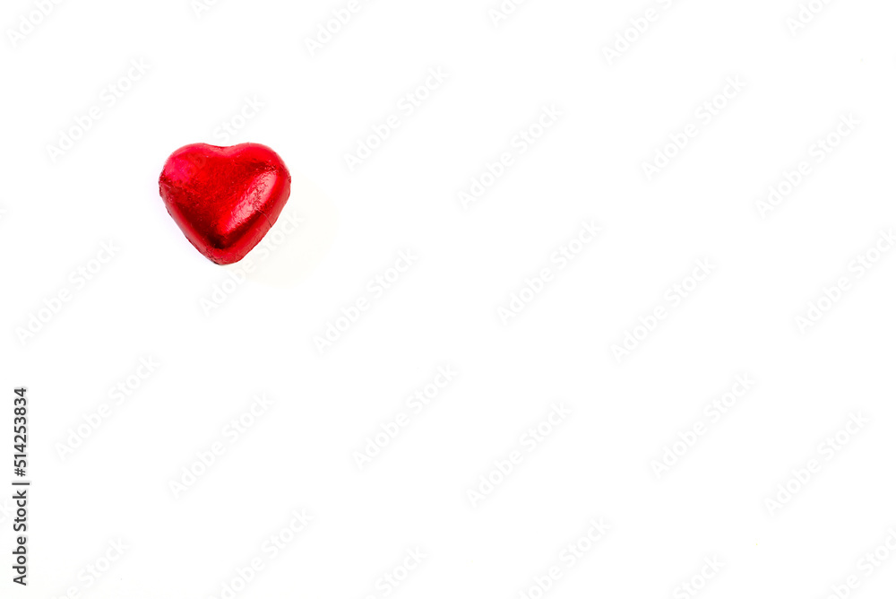 Heart shaped chocolate bonbon wrapped in red foil on a white background. copy space Heart shaped chocolate bonbon wrapped in red foil on a white background. copy space