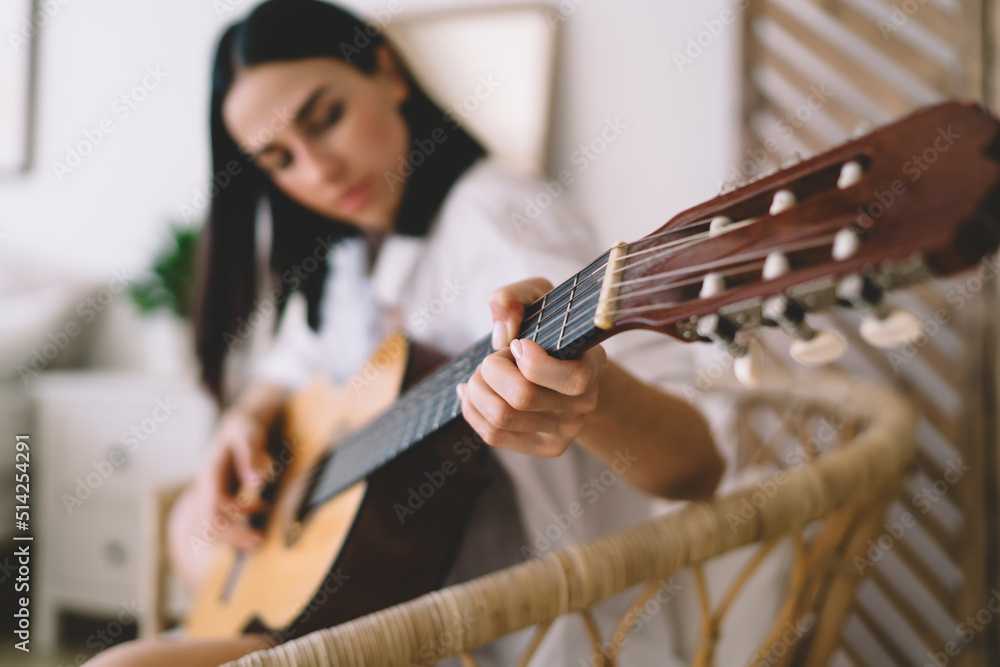 Selective focus effect, female learning to play guitar while sitting in  cozy home interior. Young concentrated woman enjoying her hobby with musical  instrument performance relaxing on wicker chair Stock Photo | Adobe