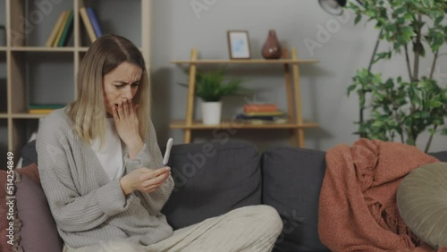 Attractive woman feeling frustration with positive pregnancy result on test stick while sitting on comfy sofa in living room. Concept of unwanted pregnancy. photo