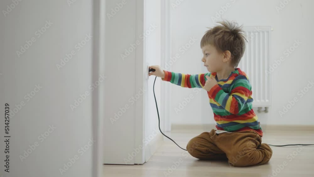 Small boy playing with electrical plug into the wall socket, unsafe ...