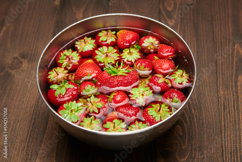 a full bowl of strawberries in water, dark wooden background, concept of fresh fruits and healthy food