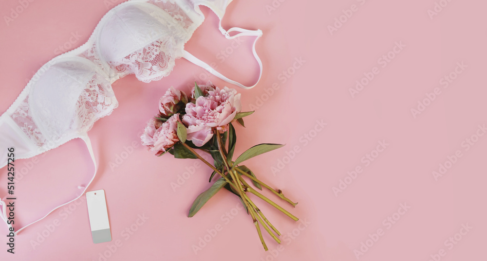 Women's white lace bra with label and peony on a pink background. Copy space. Women's white lace bra with label and peony on a pink background. Copy space.