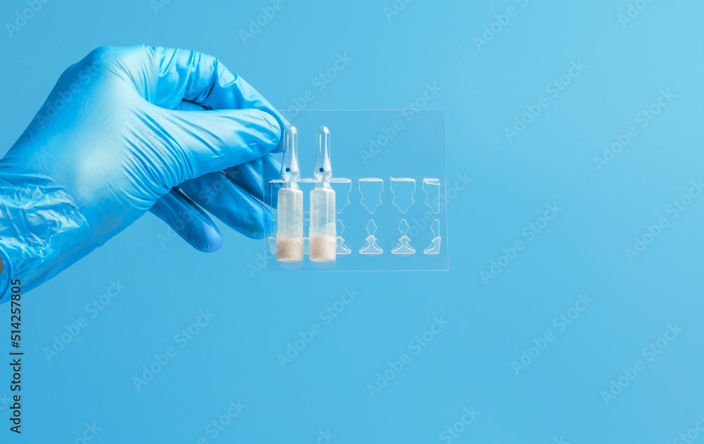Medical glove. Ampoules with a white liquid in the hand in a blue medical glove. Isolated on a blue background. Medical glove. Ampoules with a white liquid in the hand in a blue medical glove. Isolated on a blue background.