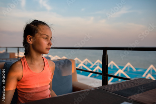 Portrait of beautiful serious girl sitting in outdoor area of café on sea shore in summer